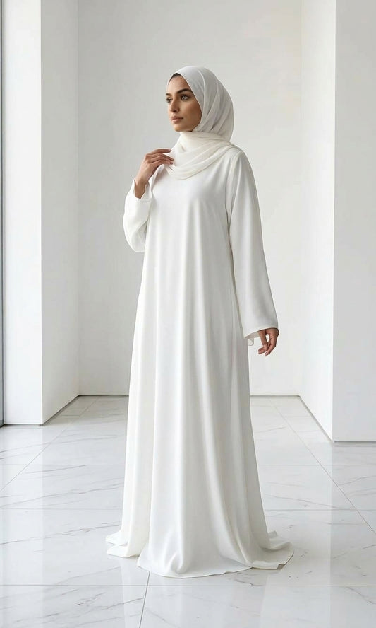 Woman wearing a long, off white colour dress and hijab standing in an indoor setting.